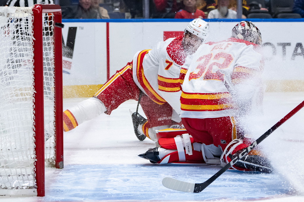 Vancouver Canucks' Filip Hronek (17) scores on Calgary Flames goaltender Dustin Wolf (32) as Kevin Bahl (7) watches during the first period of an NHL hockey game in Vancouver, British Columbia, on Sunday, Nov. 23, 2025. (Ethan Cairns/The Canadian Press via AP)