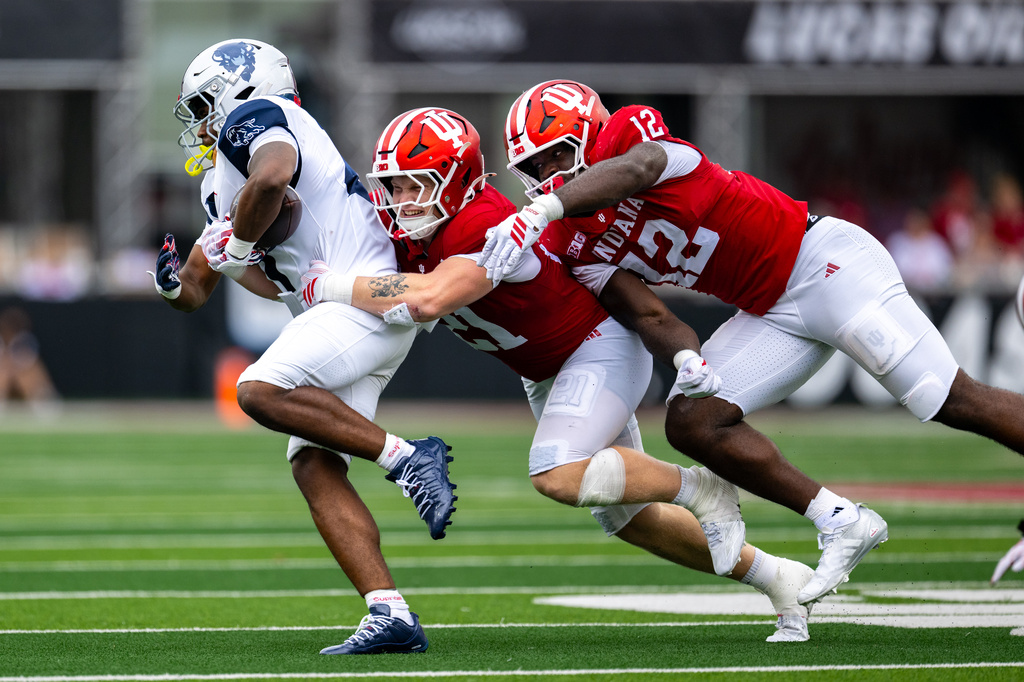 Howard running back John Washington IIl, left, is contacted by Indiana linebacker Jacob Savage, center, and defensive end Tobi Osunsanmi (12) during the second half an NCAA college football game, Saturday, Sept. 12, 2026, in Bloomington, Ind. (AP Photo/Doug McSchooler)