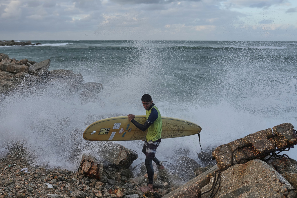 Palestinian Khalil Abu Jayyab carries his surfing board as they enter the water along a damaged shoreline in Gaza City, Sunday, Dec. 28, 2025. (AP Photo/Jehad Alshrafi)