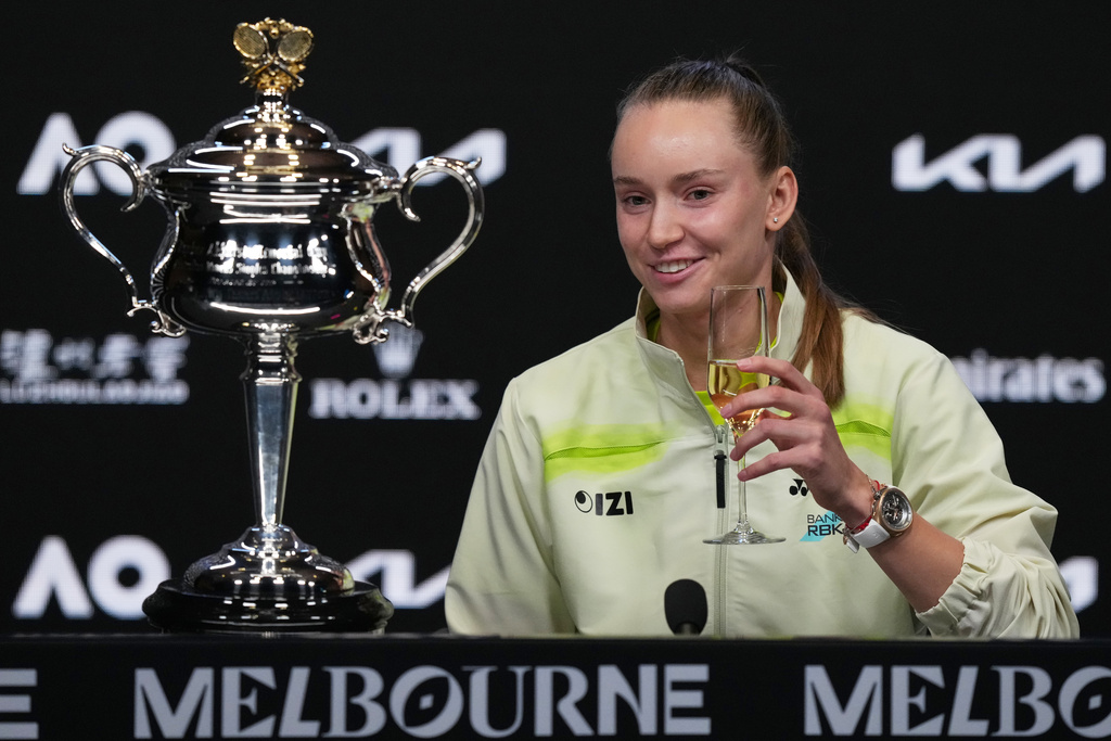 Elena Rybakina of Kazakhstan holds a glass of champagne as she sits next to the Daphne Akhurst Memorial Cup at a press conference after defeating Aryna Sabalenka of Belarus in the women's singles final at the Australian Open tennis championship in Melbourne, Australia, Saturday, Jan. 31, 2026. (AP Photo/Aaron Favila)