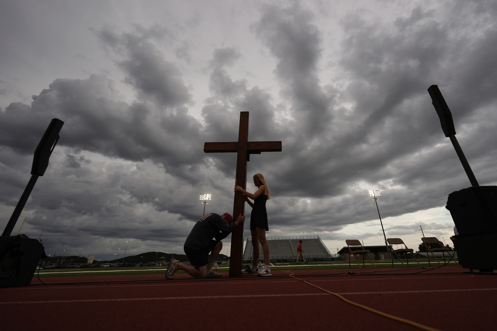 Dan Beazley, of Michigan, left, reacts as he holds a large cross with Abigail Smithson during a vigil for flooding victims at Tivy Antler Stadium on Wednesday, July 9, 2025, in Kerrville, Texas. (AP Photo/Gerald Herbert)