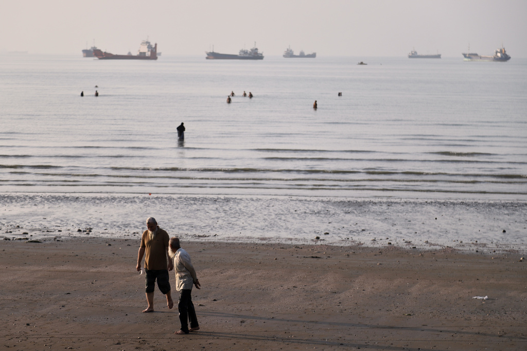 Men walk on the shoreline as people wade in the water in the Strait of Hormuz, where cargo and service vessels are anchored off Bandar Abbas, Iran, Monday, June 1, 2026. (Amirhosein Khorgooi/ISNA via AP)