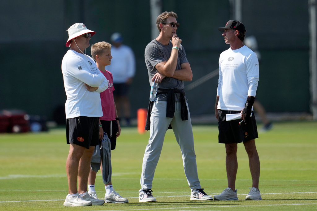 San Francisco 49ers general manager John Lynch, left, looks on as head coach Kyle Shanahan, right, talks to Golden State Warriors general manager Mike Dunleavy Jr., during a joint NFL training camp practice with the Tennessee Titans Tuesday, Aug. 11, 2026, in Santa Clara, Calif. (AP Photo/Jeff Chiu)