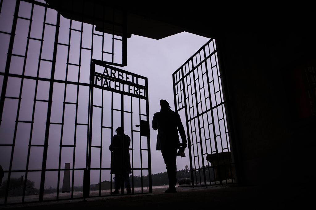 Two men enter the Nazi Concentration Camp Sachsenhausen through a gate with writing "Arbeit macht frei" in German reading "Work makes free", on the eve on the International Holocaust Memorial Day in Oranienburg, Germany, Monday, Jan. 26, 2026. (AP Photo/Markus Schreiber)