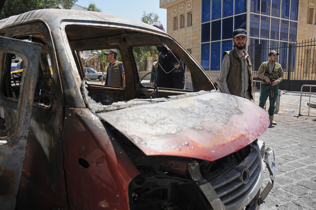 Syrian security personnel inspect a burned vehicle near the Four Seasons Hotel after two explosions rocked the area earlier while Syrian President Ahmad al-Sharaa was meeting French President Emmanuel Macron at the presidential palace, in Damascus, Syria, Tuesday, July 7, 2026. (AP Photo/Omar Albam)