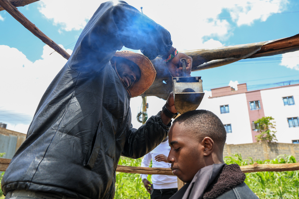 Barber and viral content creator Safari Martins, demonstrates one of his inventive shaving methods using an iron box while grooming Ian Njenga in Kiambu, Kenya, Wednesday, Nov. 26, 2025. (AP Photo/Andrew Kasuku)