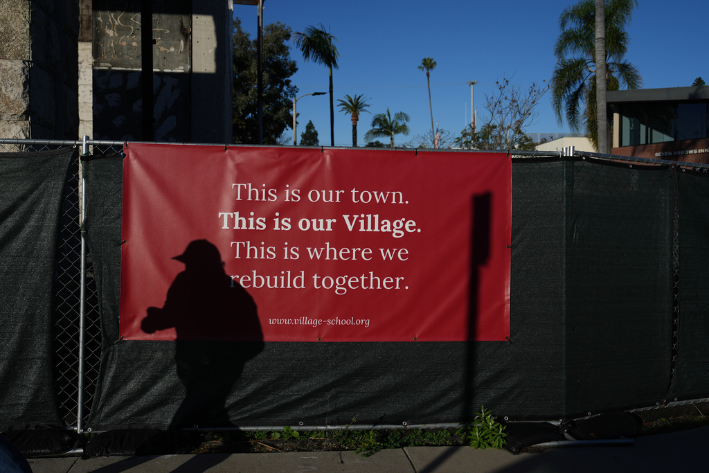 A person casts a shadow on a fence in front of a sign on the one-year anniversary of the Palisades Fire in the Pacific Palisades neighborhood of Los Angeles Wednesday, Jan. 7, 2026. (AP Photo/Jae C. Hong)