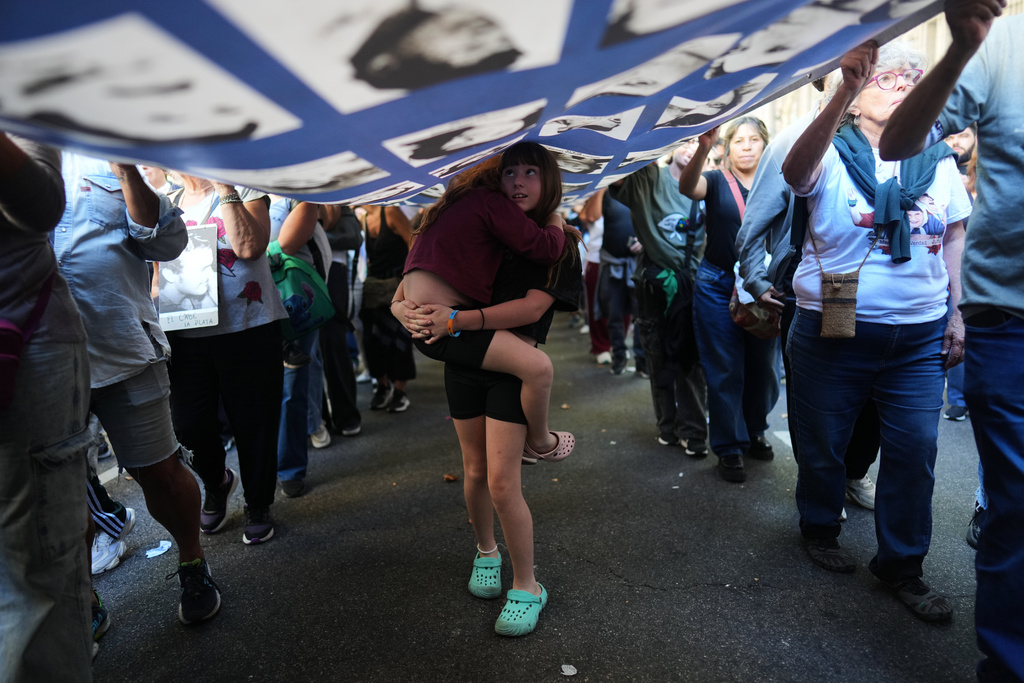 Girls walk under a banner of people who disappeared during Argentina's military dictatorship (1976–1983) during a rally on the anniversary of the coup that brought the military regime to power, in Buenos Aires, Argentina, Tuesday, March 24, 2026. (AP Photo/Rodrigo Abd)