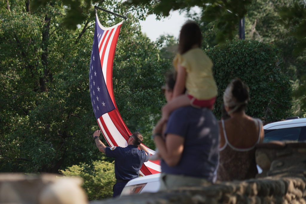 A first responder adjusts an American flag during a procession in Grand Junction, Colo., Monday, June 29, 2026, for firefighters who died battling blazes near the Colorado-Utah border. (AP Photo/Ty ONeil)