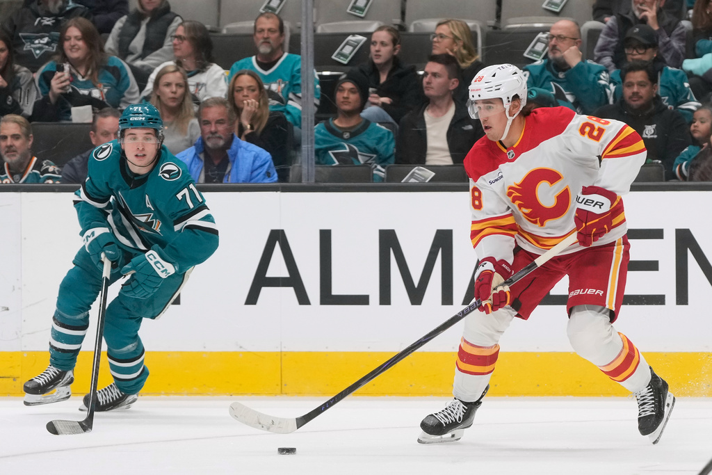 Calgary Flames defenseman Zach Whitecloud, right, skates with the puck against San Jose Sharks center Macklin Celebrini (71) during the first period of an NHL hockey game in San Jose, Calif., Thursday, Feb. 26, 2026. (AP Photo/Jeff Chiu)