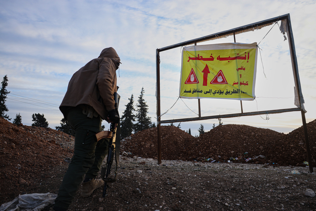 FILE - A member of the Syrian military police stands near a sign with Arabic text that reads "The road is dangerous. SDF is 1 kilometer away", at a humanitarian crossing declared by the Syrian army in the village of Hamima, in the eastern Aleppo countryside, near the front line with the Kurdish-led Syrian Democratic Forces in Deir Hafer, Syria, Thursday, Jan. 15, 2026. (AP Photo/Omar Albam)