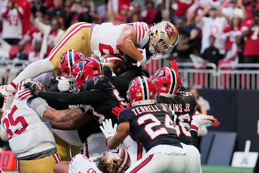 San Francisco 49ers running back Christian McCaffrey, top, leaps into the end zone over Atlanta Falcons' A.J. Terrell Jr. (24), Harold Perkins Jr. (56) and other defenders to score a touchdown during the first half of an NFL football game in Atlanta, Sunday, Oct. 25, 2026. (AP Photo/Brynn Anderson)
