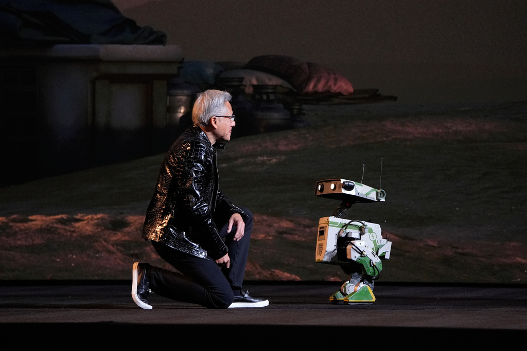 Nvidia founder and CEO Jensen Huang kneels in front of a robot during a Nvidia news conference ahead of the CES tech show Monday, Jan. 5, 2026, in Las Vegas. (AP Photo/John Locher)