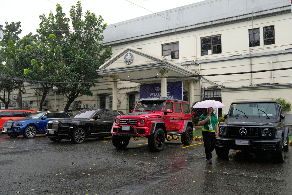 A woman passes by luxury European and British vehicles that are auctioned after they were seized from a wealthy couple accused in massive flood-control project corruptions at the Bureau of Customs in Manila, Philippines on Thursday, Nov. 20, 2025. (AP Photo/Aaron Favila)
