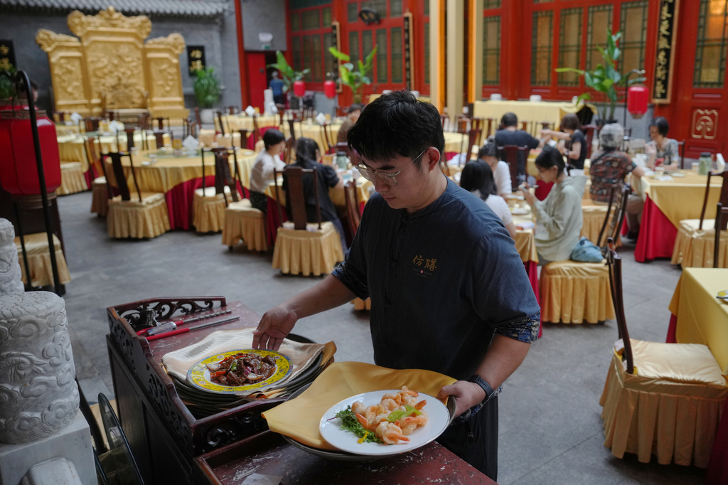 A waiter prepares to serve dishes for customers at Fangshan Restaurant in Beijing on July 23, 2026. (AP Photo/Andy Wong)