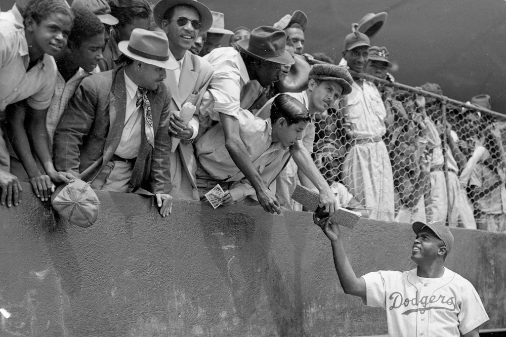 FILE - Jackie Robinson, first baseman of the Brooklyn Dodgers, returns an autograph book to a fan in the stands, during the Dodgers' spring training in Ciudad Trujillo, now Santo Domingo, in the Dominican Republic, on March 6, 1948. (AP Photo/File)
