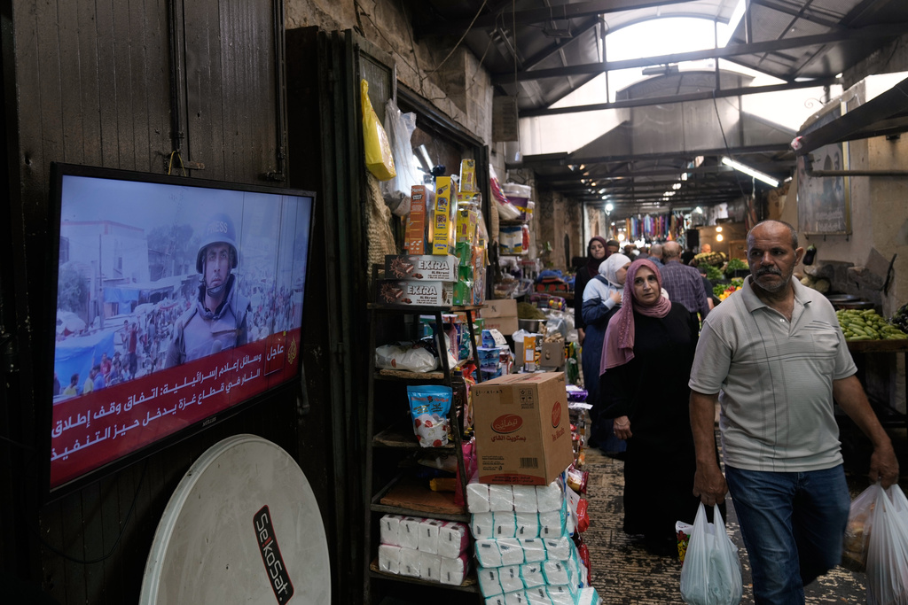 A Palestinian man looks at a television broadcasting the news following the announcement that Israel and Hamas have agreed to the first phase of a peace plan to pause the fighting, as he walks at a local market in the Old City of Nablus, in the West Bank, Thursday, Oct. 9, 2025. (AP Photo/Majdi Mohammed)