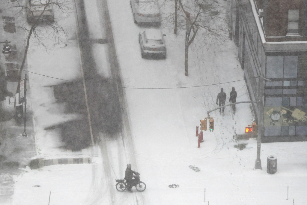 Pedestrians walk and ride their bike as heavy snow falls, Sunday, Jan. 25, 2026, in New York. (AP Photo/Heather Khalifa)