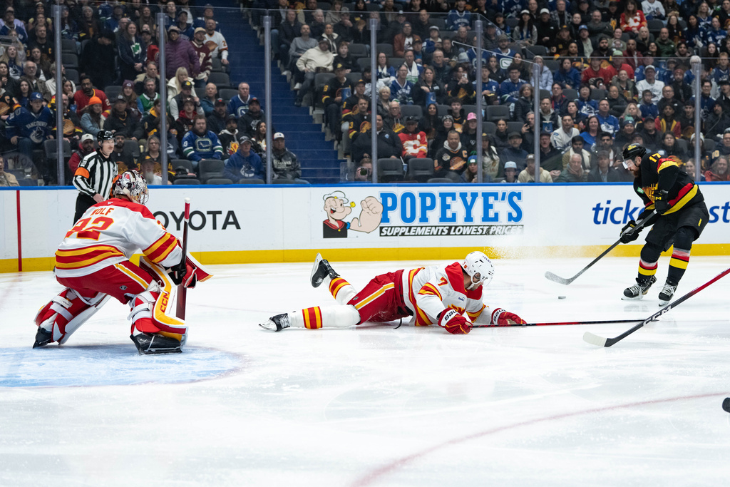 Vancouver Canucks' Filip Hronek (17) shoots the puck to score on Calgary Flames goaltender Dustin Wolf as Kevin Bahl defends during the first period of an NHL hockey game in Vancouver, British Columbia, on Sunday, Nov. 23, 2025. (Ethan Cairns/The Canadian Press via AP)