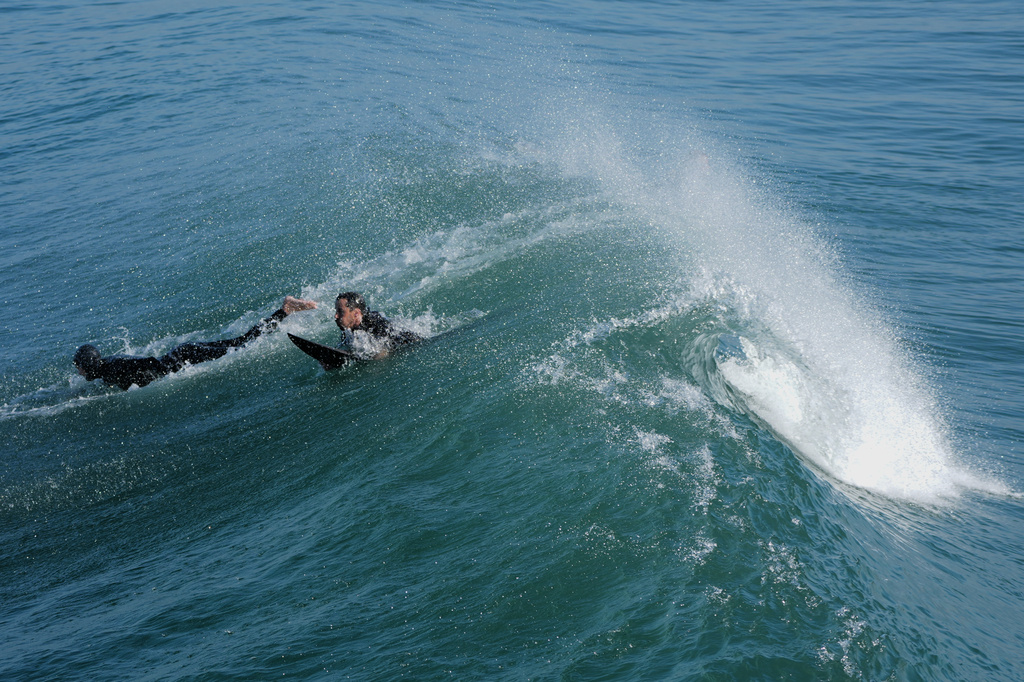 Surfers pass under a wave alongside the Imperial Beach pier Wednesday, March 11, 2026, in Imperial Beach, Calif. (AP Photo/Gregory Bull)