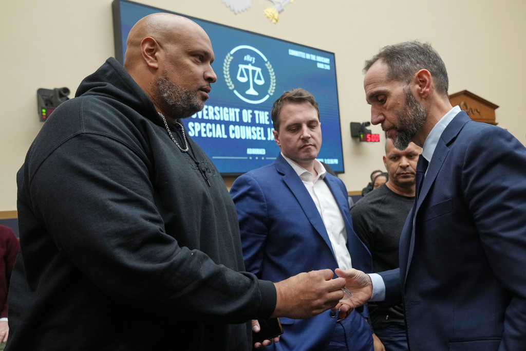Former U.S. Capitol Police Sgt. Harry Dunn, left, hands former Justice Department special counsel Jack Smith a police patch after the House Judiciary Committee hearing about his investigations into President Donald Trump at the Capitol in Washington, Thursday, Jan. 22, 2026. Looking on at center is Washington Metropolitan Police officer Daniel Hodges. (AP Photo/Jacquelyn Martin)