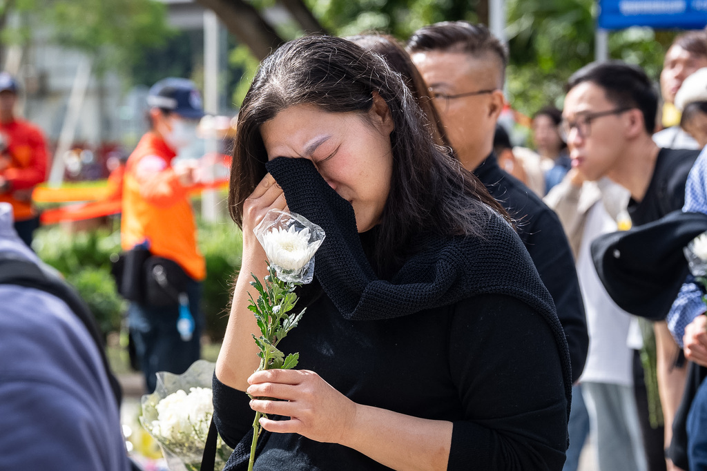 People react as they offer flowers for the victims near the site of a deadly fire at Wang Fuk Court, a residential estate in the Tai Po district of Hong Kong's New Territories on Tuesday, Dec 2, 2025. (AP Photo/Chan Long Hei)