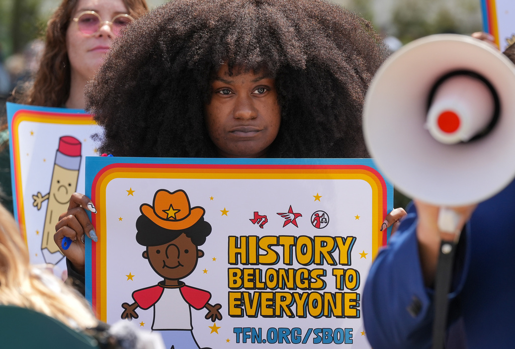 Taylor Crawford of Houston holds a sign reading "History belongs to everyone" during a rally on the Capitol Mall outside the Barbara Jordan State Office Building, where the State Board of Education meets, Tuesday, April 7, 2026, in Austin, Texas. (Jay Janner/Austin American-Statesman via AP)