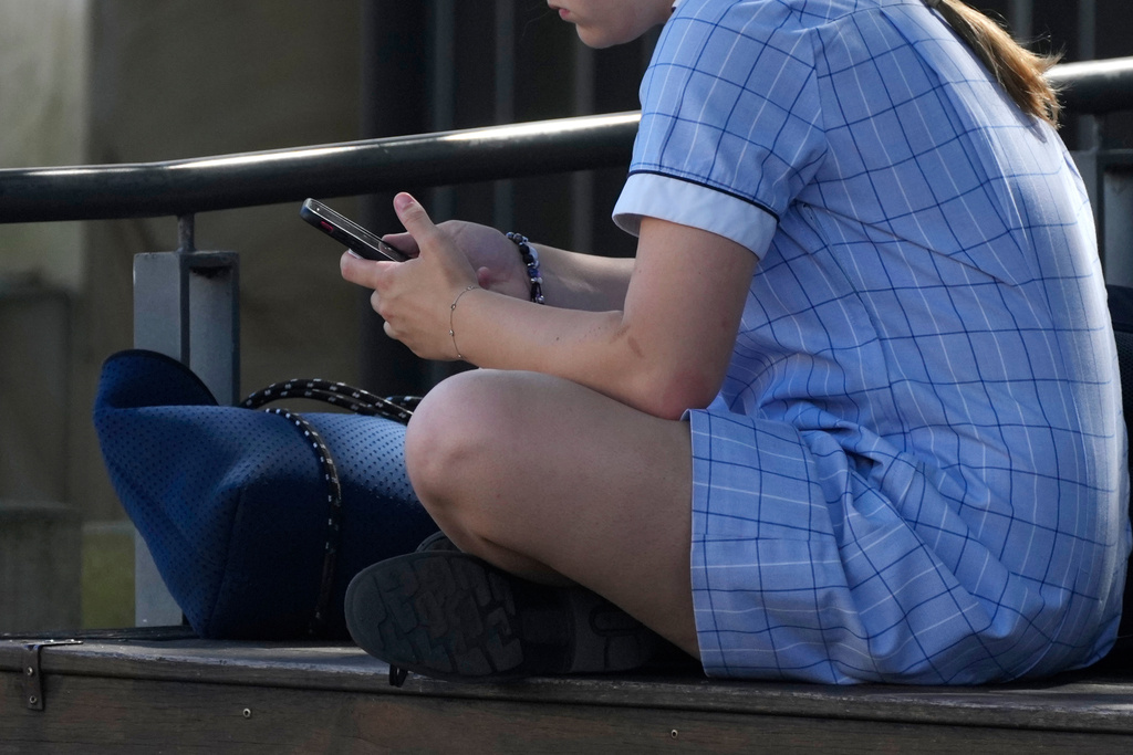 FILE - A young girl uses her phone while sitting on a bench in Sydney, on Nov. 8, 2024. (AP Photo/Rick Rycroft, File)