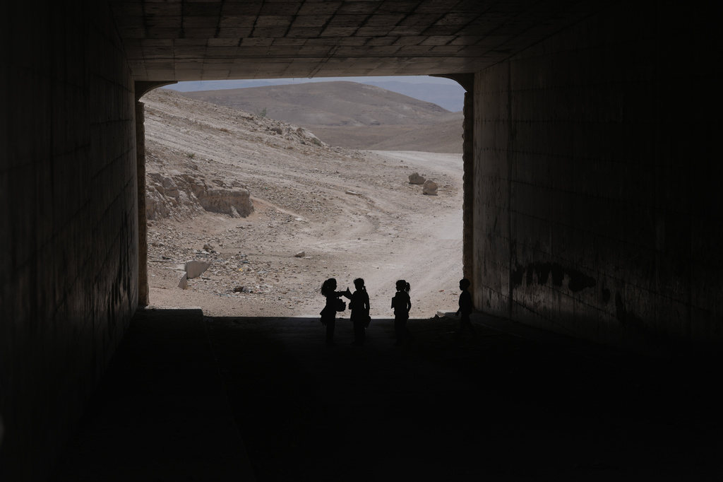 Palestinian children go through a vehicles tunnel on their way home, after receiving their year end reports from their school, in the West Bank Bedouin hamlets of Khan al-Ahmar, Wednesday, June 10, 2026. (AP Photo/Mahmoud Illean)