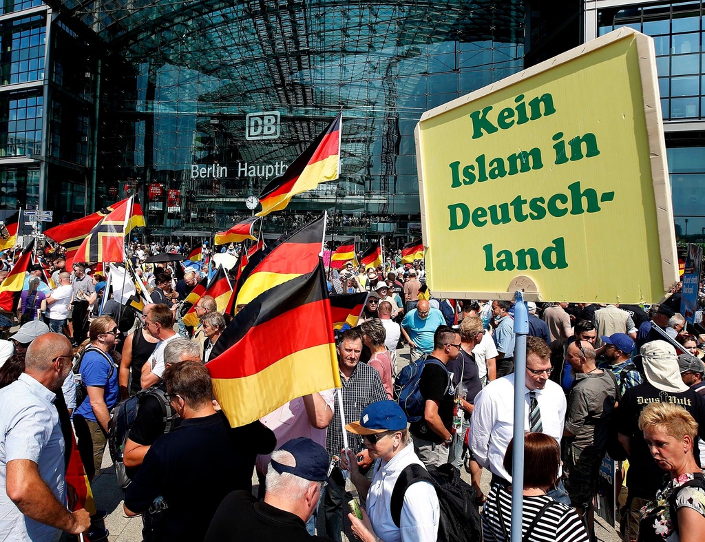 FILE - Supporters of the Alternative for Germany party wave flags in front of the train station in Berlin, May 27, 2018. The poster reads, "No Islam in Germany." (AP Photo/Michael Sohn, File)