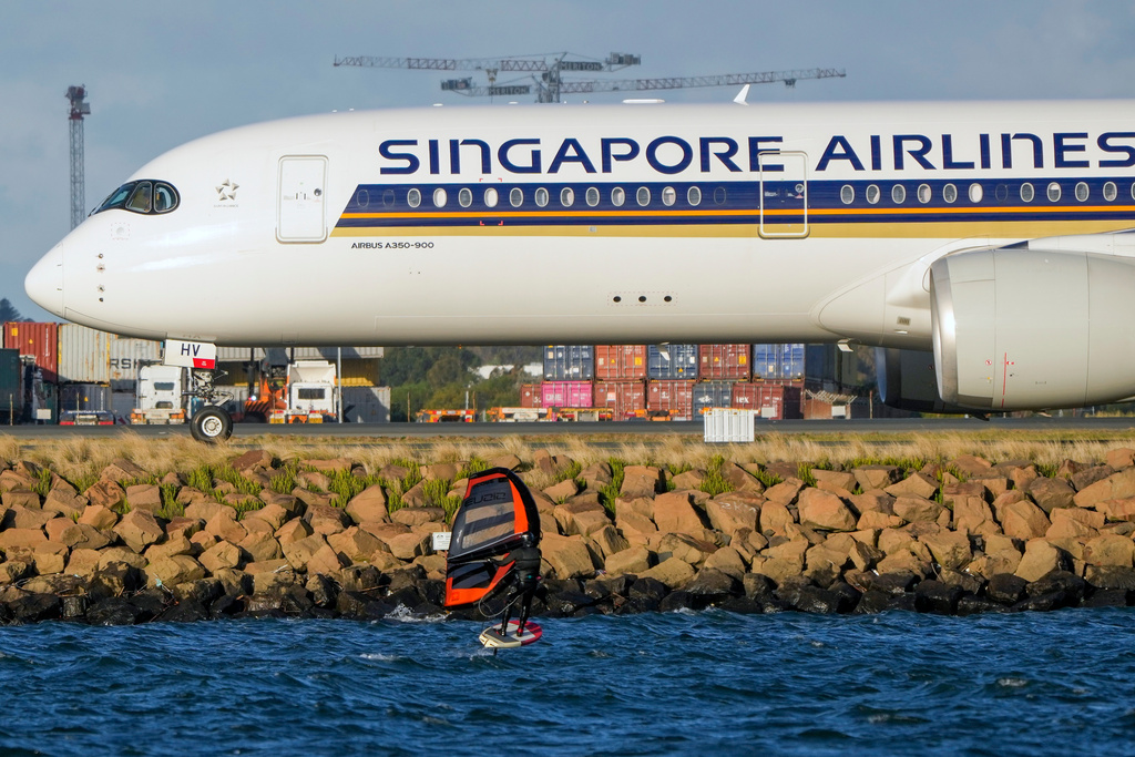 FILE - A man wing foils on Botany Bay as a Singapore Airlines passenger jet taxis after landing at Sydney Airport in Australia, Sept. 5, 2022. (AP Photo/Mark Baker, File)