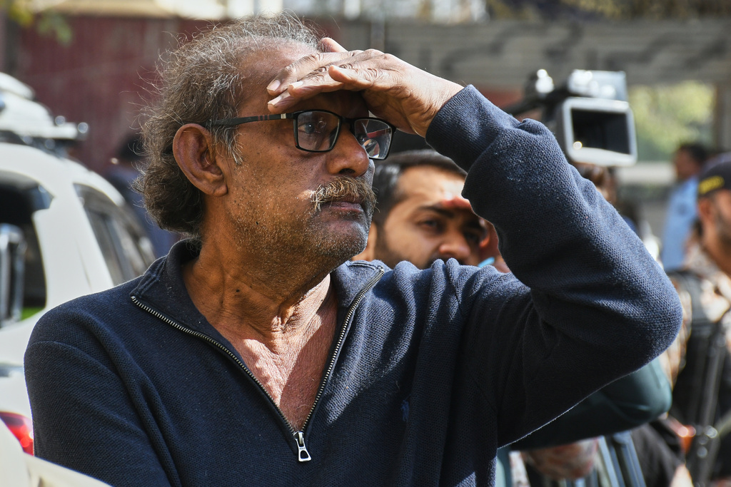 A family member of a missing person waits as rescue workers and firefighters search through the rubble of a burnt building of a multistory shopping plaza following a massive fire in Karachi, Pakistan, Tuesday, Jan. 20, 2026. (AP Photo/Ali Raza)
