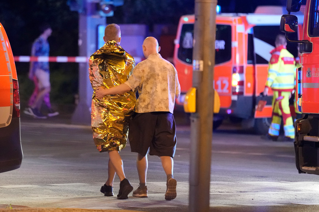 Two people walk together past emergency vehicles in Berlin, early Sunday, July 26, 2026, following the cancellation of Christopher Street Day festivities. (AP Photo/Markus Schreiber)