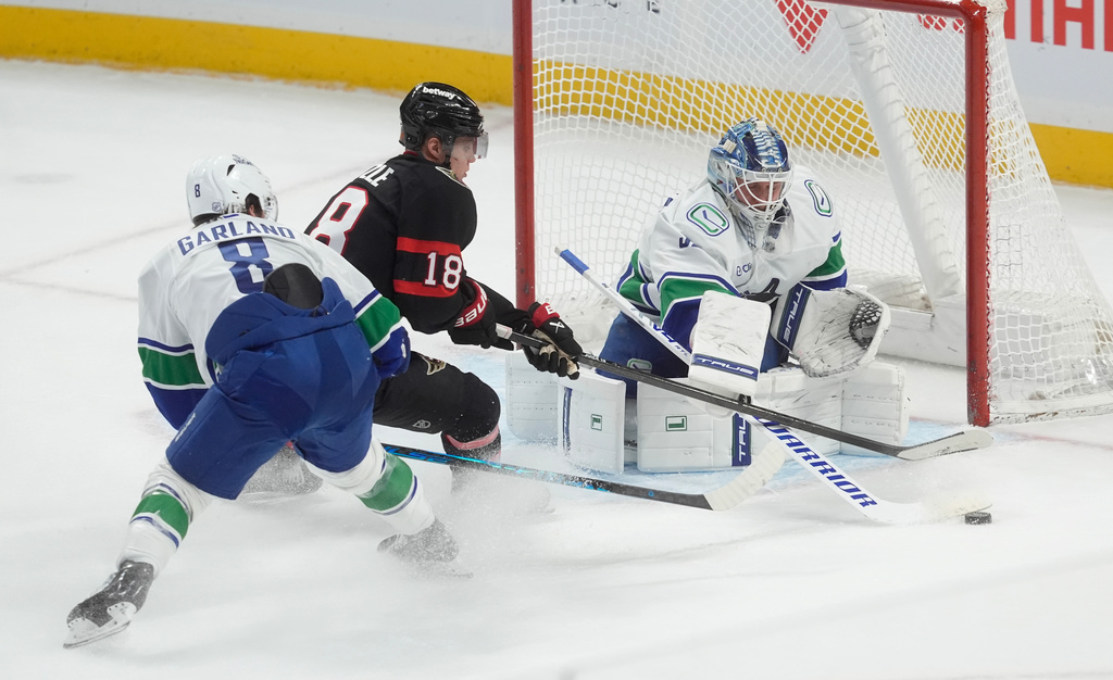 Vancouver Canucks goaltender Kevin Lankinen (32) poke checks the puck away from Ottawa Senators center Tim Stutzle (18) as he is pressured by Canucks right wing Conor Garland (8) during second period NHL action in Ottawa, Tuesday, Jan. 13, 2026. (Adrian Wyld/The Canadian Press via AP)