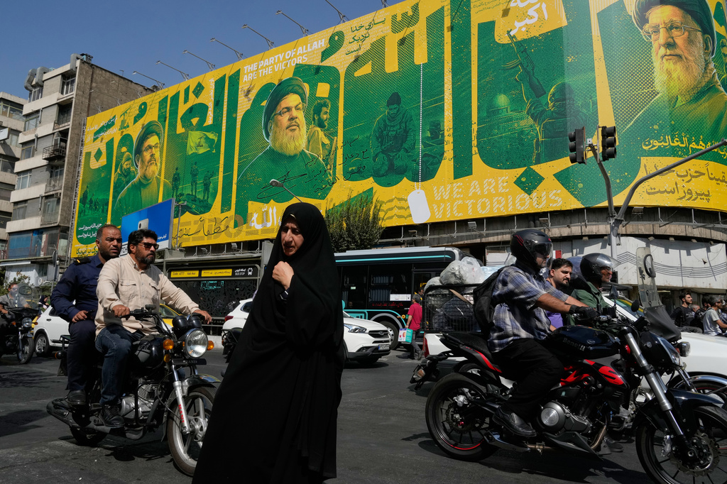 A woman walks and vehicles drive in an intersection in front of a billboard showing portraits of the late Iranian Supreme Leader Ayatollah Ali Khamenei, right, late leaders of Lebanon's Hezbollah group Hassan Nasrallah, center left, and Hashem Safieddine, left, marking the second anniversary of the killing of Hassan Nasrallah, in Tehran, Iran, Sunday, Sept. 27, 2026. (AP Photo/Vahid Salemi)