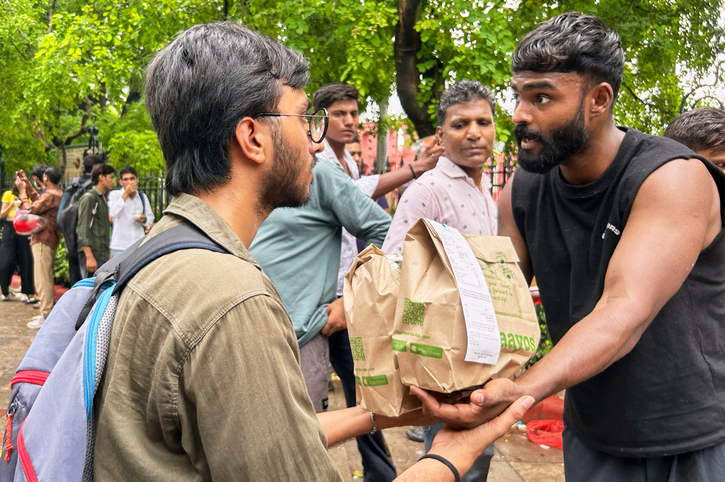 A protestor, left, receives a food package from a supporter at the site where thousands have assembled to join a protest led by Cockroach Janta Party in New Delhi, India, Wednesday, July 22, 2026. (AP Photo/Piyush Nagpal)