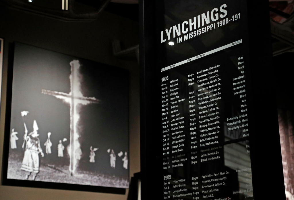 FILE - A monolith listing the names, dates and rationale for the lynching of African-American residents rests in the foreground of a photograph of a burning Ku Klux Klan cross on display in the Mississippi Civil Rights Museum in Jackson, Miss, Nov. 10, 2017. (AP Photo/Rogelio V. Solis, file)