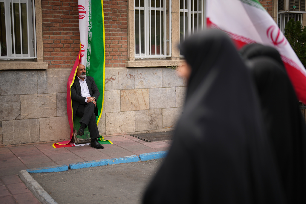 A man leans against an Iranian flag banner during a government-sponsored protest attended by medical workers against the U.S.-Israeli military campaign outside Imam Khomeini Hospital in Tehran, Iran, Monday, April 6, 2026. (AP Photo/Francisco Seco)