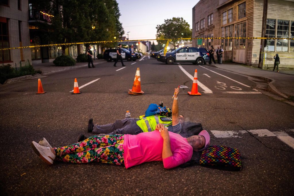 People relax on a street outside a U.S. Immigration and Customs Enforcement facility on Tuesday, Oct. 7, 2025, in Portland, Ore. (AP Photo/Ethan Swope)