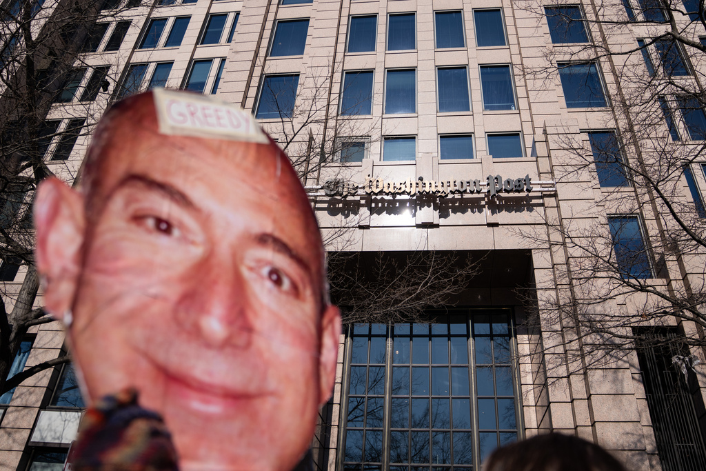A protester holds a cutout of Jeff Bezos' face outside of the Washington Post office following a mass layoff, Thursday, Feb. 5, 2026, in Washington. (AP Photo/Allison Robbert)