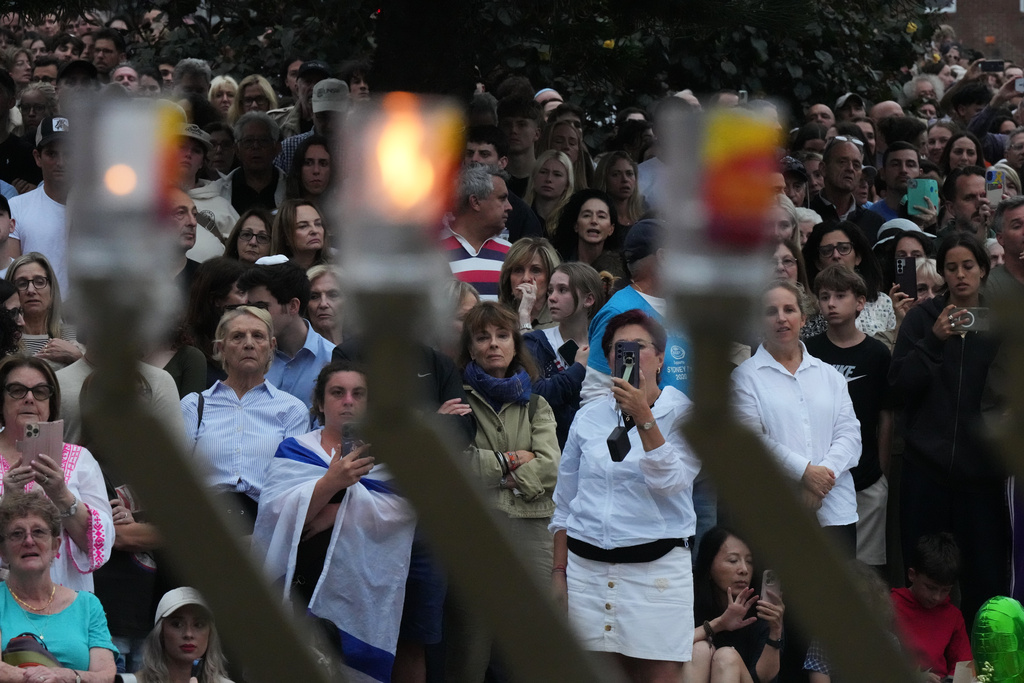 People attend a menorah lighting ceremony at a floral memorial for victims of Sunday's shooting, at the Bondi Pavilion on Bondi Beach on Tuesday, Dec. 16, 2025, in Sydney, Australia. (AP Photo/Mark Baker)