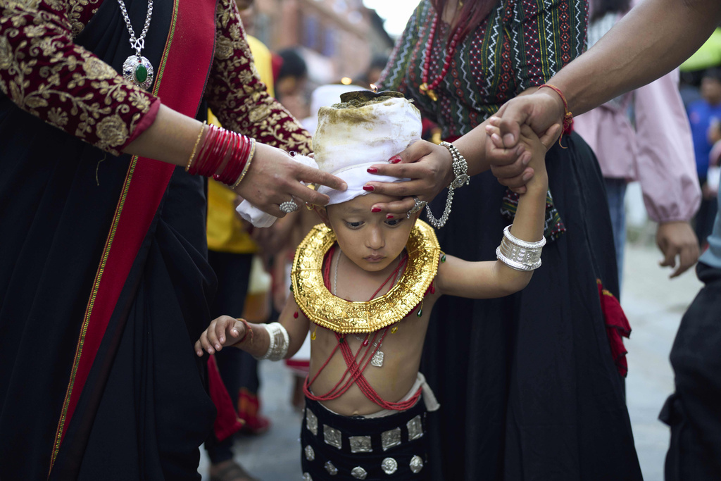 Devotees adjust a lighted oil lamp on the head of a child during a parade celebrating the birthday of Lord Krishna on Krishna Janmashtami festival in Bhaktapur, Nepal, Saturday, Aug. 16, 2025. (AP Photo/Niranjan Shrestha)