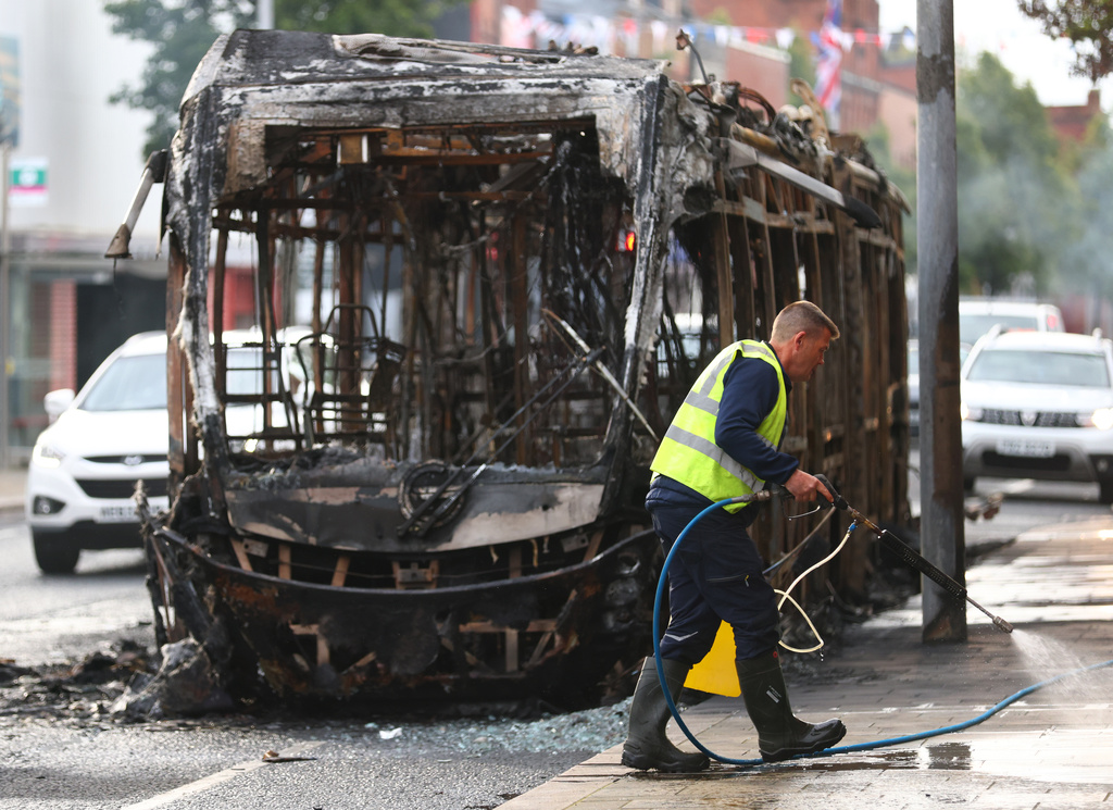A worker clear up the debris in front of a burnt out bus, after rioting broke out late Tuesday, in east Belfast, Northern Ireland, Wednesday, June 10, 2026, following a stabbing incident. (AP Photo/Peter Morrison)