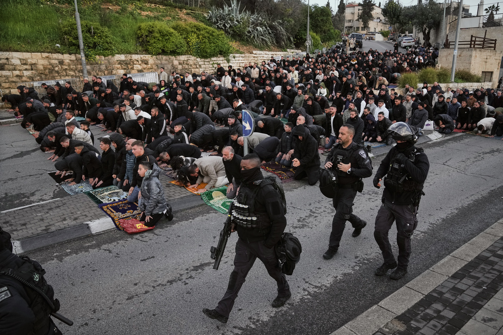 Israeli police officers pass by Palestinian Muslims as they offer Eid al-Fitr prayers in Jerusalem while the Old City remains closed to visitors under nationwide Home Front Command restrictions banning large gatherings amid the war with Iran, Friday, March 20, 2026. (AP Photo/Mahmoud Illean)