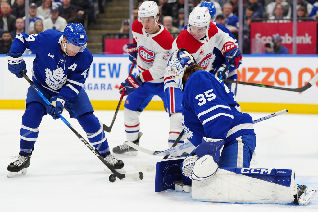 Toronto Maple Leafs defenceman Morgan Rielly (44) clears the puck from in front of his goalie Dennis Hildeby (35) as Montréal Canadiens left wing Juraj Slafkovský (20) and Canadiens right wing Cole Caufield (13) look on during first period NHL hockey action in Toronto on Saturday, Dec. 6, 2025. (Frank Gunn/The Canadian Press via AP)