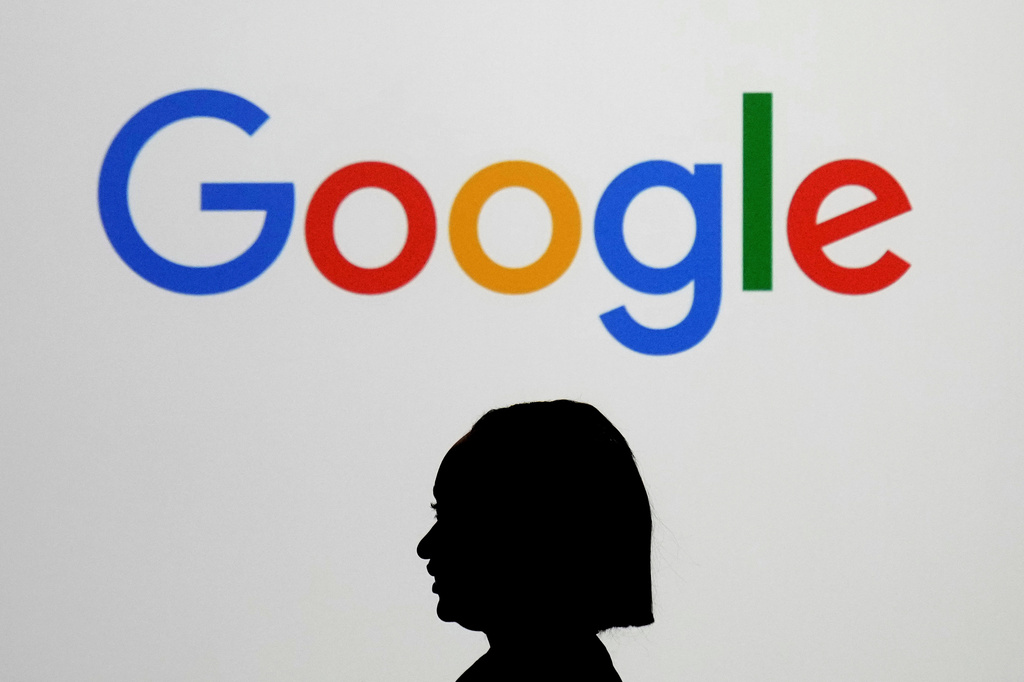 FILE - A woman walks by a giant screen displaying the Google logo at an event at the Paris Google Lab on the sidelines of the AI Action Summit in Paris, Feb. 9, 2025. (AP Photo/Thibault Camus, File)