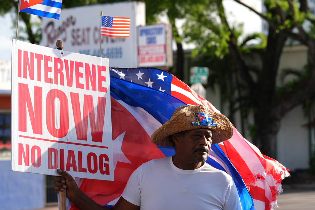 Santiago Ferran holds a sign calling for American intervention in Cuba, as a small group of Cubans turned out to wave flags and hold signs hours after federal prosecutors announced charges against Castro in the 1996 downing of civilian planes operated by Miami-based exiles, Wednesday, May 20, 2026, in Miami. (AP Photo/Rebecca Blackwell)