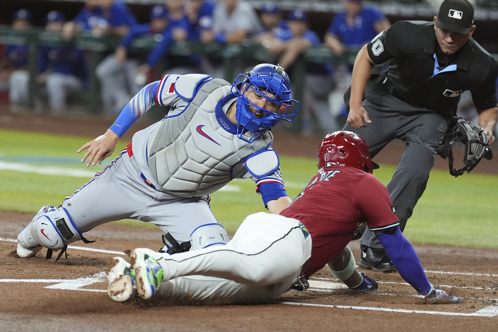 Texas Rangers catcher Kyle Higashioka, left, tags out Arizona Diamondbacks' Ketel Marte at home plate as home plate umpire Roberto Ortiz, right, looks on during the first inning of a baseball game Wednesday, Sept. 3, 2025, in Phoenix. (AP Photo/Ross D. Franklin)