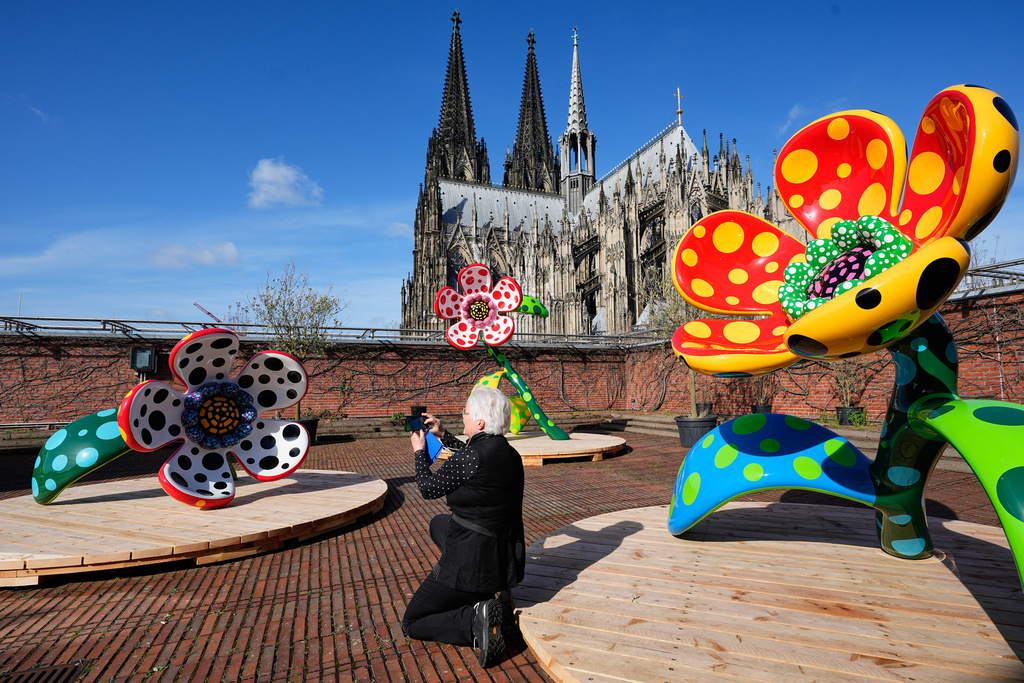 A woman takes pictures of the artwork 'Flowers that speak all about my heart given to the sky' in front of the Cologne Cathedral during a preview of the new major exhibition of legendary Japanese artist Yayoi Kusama at the Museum Ludwig in Cologne, Thursday, March 12, 2026. (AP Photo/Martin Meissner)