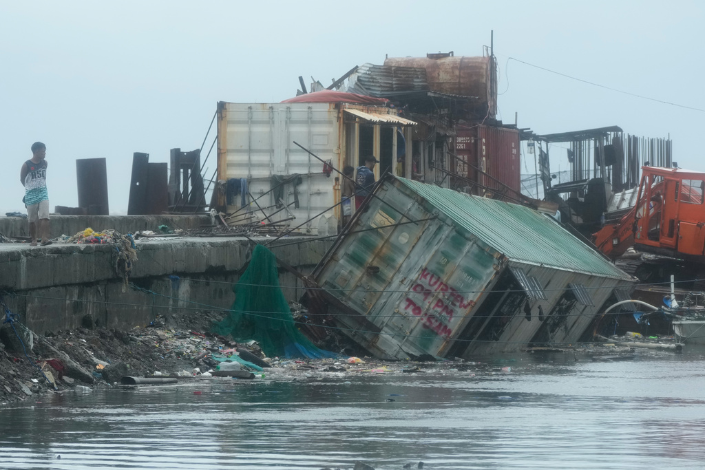 A man walks beside a container van that was toppled due to strong winds and waves caused by Typhoon Fung-wong on Monday, Nov. 10, 2025, along a coastal town in Navotas, Philippines. (AP Photo/Aaron Favila)